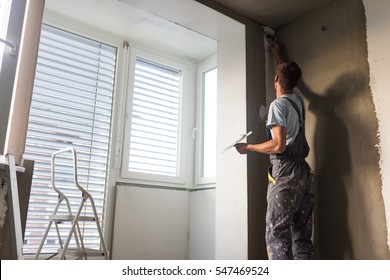 Construction worker wearing worker overall with wall plastering tools renovating apartment house. Plasterer renovating indoor walls and ceilings with float and plaster. Construction finishing works.