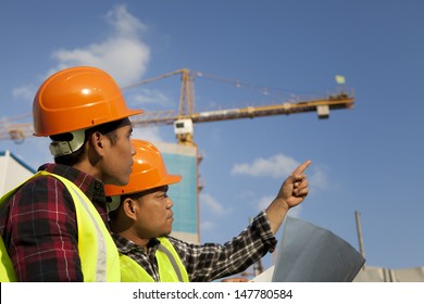 Construction worker wearing protective clothing discussion on location site and yellow crane on the background