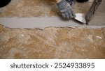 Construction worker wearing protective gloves is applying cement glue mixture on the floor using trowel.