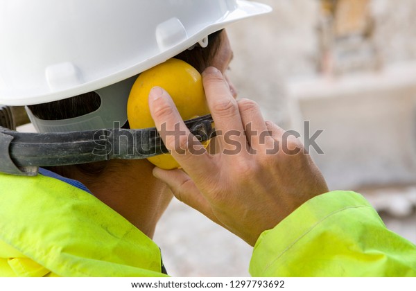 Construction worker wearing protective hard hat\
and ear defenders