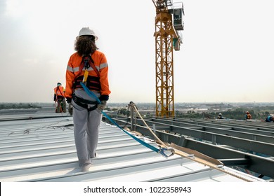 Construction worker wearing safety harness and safety line working on a metal industry roof new warehouse