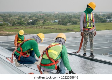 Construction worker wearing safety harness and safety line working on a metal industry roof new warehouse