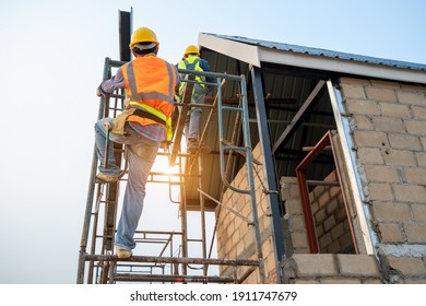 Construction worker wearing safety harness and safety line working on scaffolding at new house under construction.