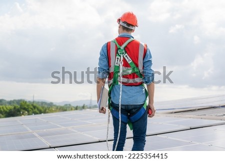 Construction worker wearing safety harness and safety line working on solar cell on roof factory.