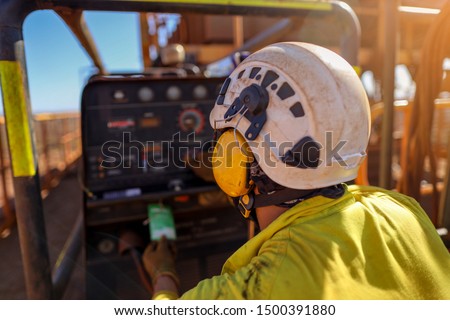 Construction worker wearing side impact rope access safety white helmet attached with yellow noise disruptive earmuffs protection while inspecting working near generator prior performing work 