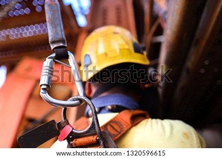 Construction worker welder wearing safety helmet, fall arrest harness clipping locking Karabiner which attached  retraceable shock absorber lanyard device on the back of his safety harness loop 