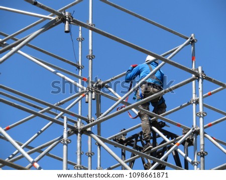 Construction worker working on scaffolding. Steeplejack on the background of clear blue sky