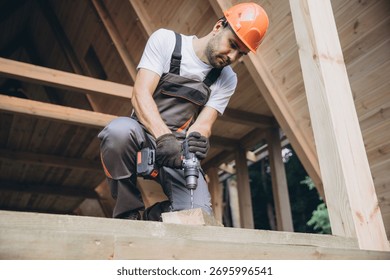 Construction worker working with screwdriver on wooden frame, diy eco-friendly homes concept. Man using drill working on construction of wood modular house