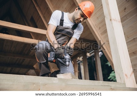 Construction worker working with screwdriver on wooden frame, diy eco-friendly homes concept. Man using drill working on construction of wood modular house