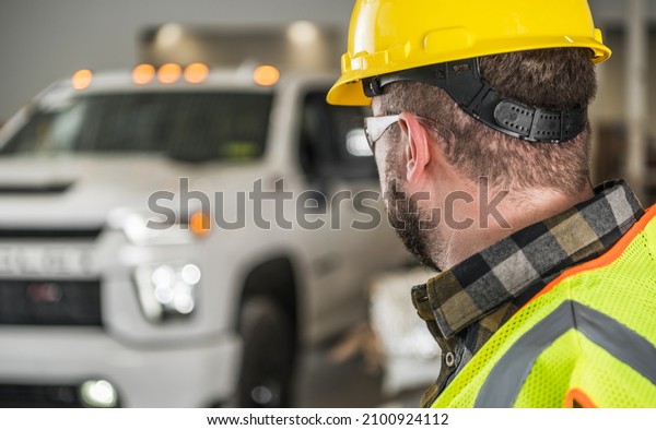 Construction Worker\
in Yellow Hard Hat and Eyes Protection Glasses Looking at His Brand\
New Commercial Pickup\
Truck