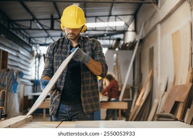 Construction worker in a yellow hardhat and safety glasses inspecting a board of wood. Ideal for carpentry, woodworking, and quality control, highlighting craftsmanship in the workshop. Labor day - Powered by Shutterstock