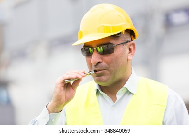 Construction Worker With Yellow Jacket And Hardhat Taking A Break From Work And Smoking Electronic Cigarette