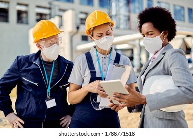 Construction workers and African American civil engineer wearing protective face masks while working on touchpad at construction site. - Powered by Shutterstock