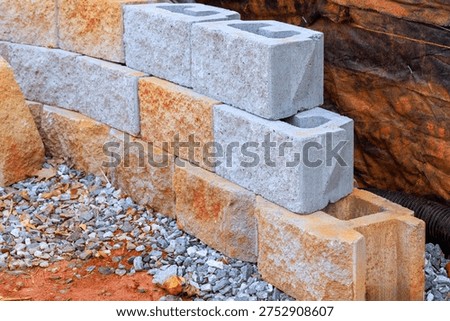 Construction workers build wall using gray an retaining blocks at work site with gravel nearby