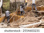 Construction workers building wooden formwork for a concrete foundation on a busy site. The image highlights teamwork, manual labor, and the detailed process of groundwork and infrastructure building.