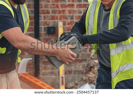 Construction workers collaborating on bricklaying project at residential site in afternoon sunlight