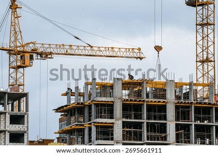 Construction workers developing a high-rise building with a towering crane lifting materials against an overcast sky, showing urban growth and engineering