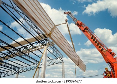 Construction workers are driving cranes to use cranes to lift large roof panels to install roofs on steel roof structures at the construction site.