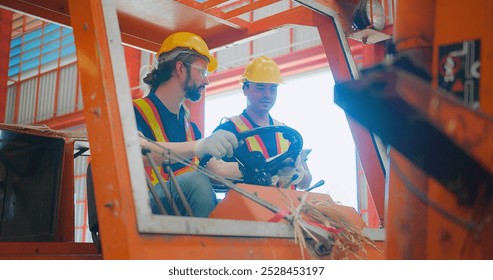 Construction workers engineers in yellow hard hats and safety vests are discussing operate a construction lift machinery within an industrial environment, focus on occupational safety and teamwork - Powered by Shutterstock