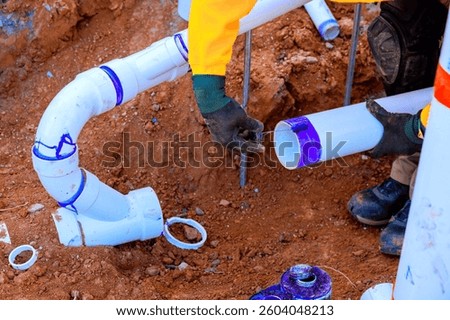 Construction workers are fitting PVC pipes together in trench, ensuring secure connection for plumbing wastewater installation.