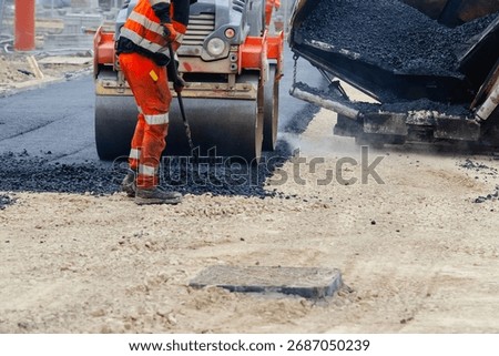 Construction workers in high-visibility gear are applyin gfresh hot asphalt to roadway surface