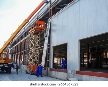 Construction workers installing facade panels on a building using a lift, with a crane nearby, capturing an active construction site.