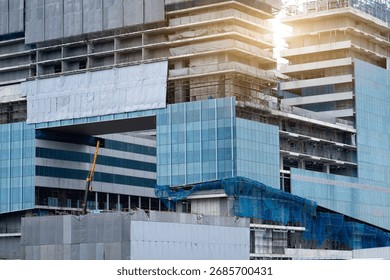 Construction workers are installing glass panels and completing structural details on a modern building. Sunlight reflects off the glass, highlighting the busy activity at the site.