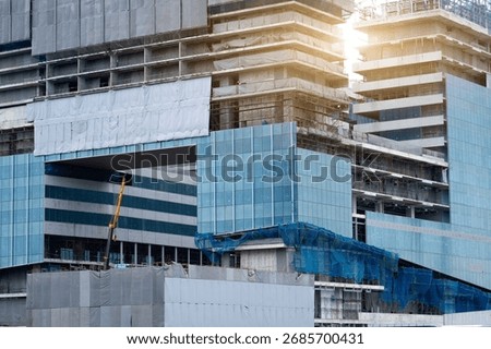 Construction workers are installing glass panels and completing structural details on a modern building. Sunlight reflects off the glass, highlighting the busy activity at the site.