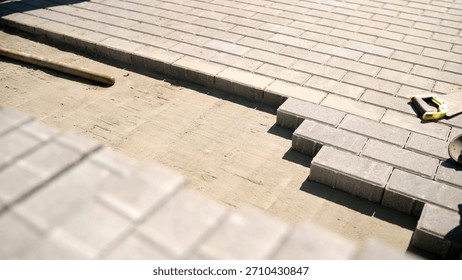 Construction workers installing gray interlocking pavers on a sand base for a new patio or driveway surface