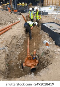 Construction workers installing underground drainage system with pipes and gravel bedding. Infrastructure development and site preparation.