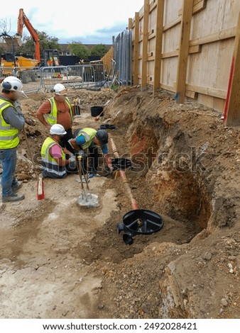 Construction workers installing underground drainage system with pipes and gravel bedding. Infrastructure development and site preparation.