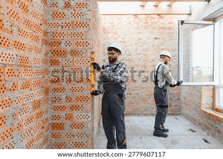 Construction workers installing a window and checking the brick wall with a spirit level on a building site