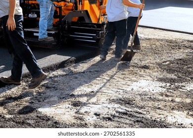 Construction workers lay asphalt using heavy machinery while others prepare surface