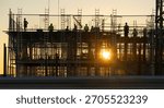 Construction workers on scaffolding making a formwork on a building site at sunset.