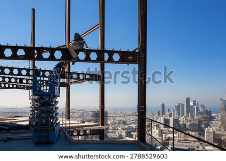Construction workers on steel framework high above Tel Aviv skyline on a clear sunny day