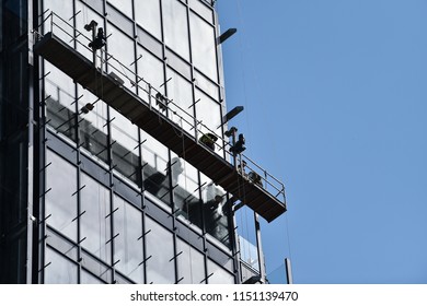 Construction workers on a suspended platform on a skyscraper glass facade