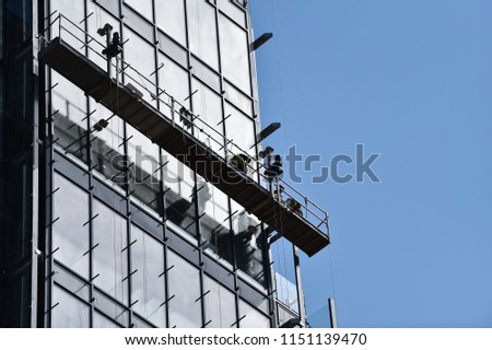 Construction workers on a suspended platform on a skyscraper glass facade