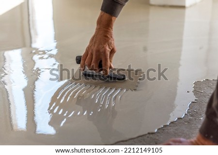 Construction workers are painting the floor using the method self-leveling epoxy.spreading self leveling compound with trowel.Self-leveling epoxy. Leveling with a mixture of cement floors.