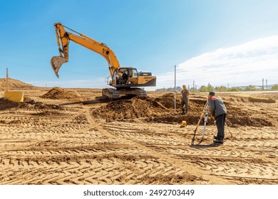 Construction workers performing land surveying and excavation tasks at a construction site under clear blue skies