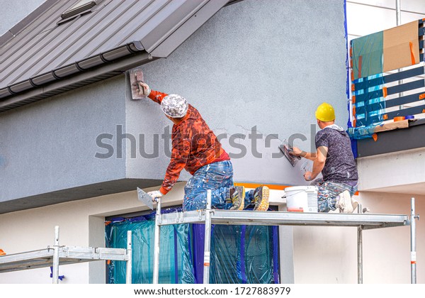 Construction workers plaster the facade of the\
house. Application Of Facade\
Plaster.