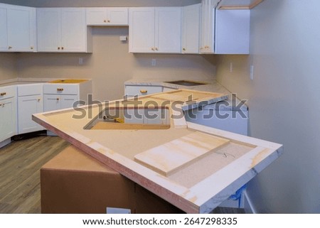 Construction workers prepare to install marble countertop in contemporary kitchen with white cabinets.