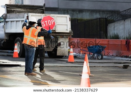 Construction workers with reflective vests and helmets holding a stop sign to organize traffic. Risk prevention work