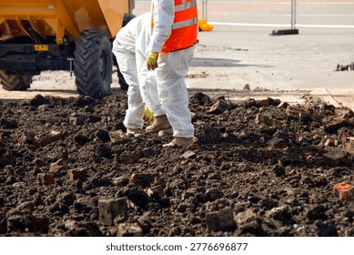 Construction workers are seen on a construction site during the afternoon. They are moving through dirt and bricks while machinery operates in the background.