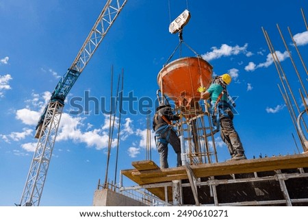 Construction workers are unloading conical metal bucket, transport and deliver cement mixture high, pouring concrete into tall vertical mold for building's pillars, use crane as he carry cone tank.