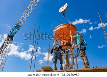 Construction workers are unloading conical metal bucket, transport and deliver cement mixture high, pouring concrete into tall vertical mold for building's pillars, use crane as he carry cone tank.