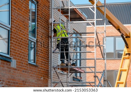 Construction workers using aluminium mobile scaffold tower and safety harness to work at height. Working at height safety regulation