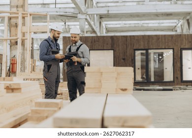 Construction workers using digital tablet while inspecting building materials in modular building factory