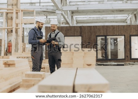 Construction workers using digital tablet while inspecting building materials in modular building factory
