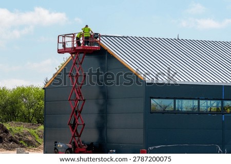 Construction workers using self propelled scissor lift to install metal roof panels on modern industrial building exterior