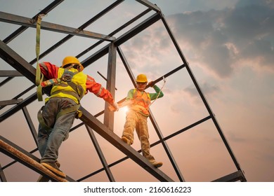 Construction workers wear safety belts during work on building roof structures at the construction site - Shutterstock ID 2160616223